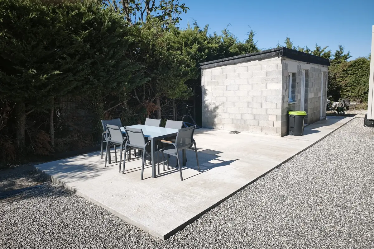 Terrasse en dalle béton finie et meublée, le long d’un local en parpaing